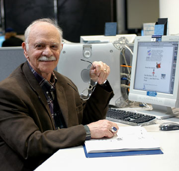 photo of Frank Christ, LSCHE co-founder, sitting at computer  desk and holding his glasses in his left hand.