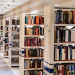 Photo by Pixabay of library book shelves down a corridor. Source: Pexels.